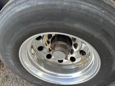 Trailer wheel with polished steel rim and tire showing hub, brake drum, and yellow hydraulic line nearby.