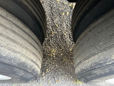 Two large trailer tires side by side with a gravel ground between them, worn tread visible.
