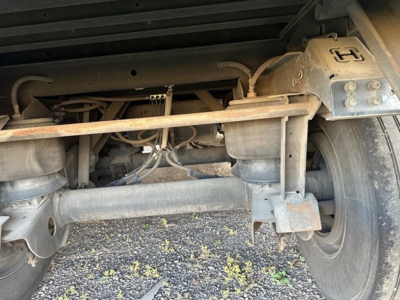 Trailer rear undercarriage showing air ride system components and suspension, with metal frame, axles, hoses, and tire visible.