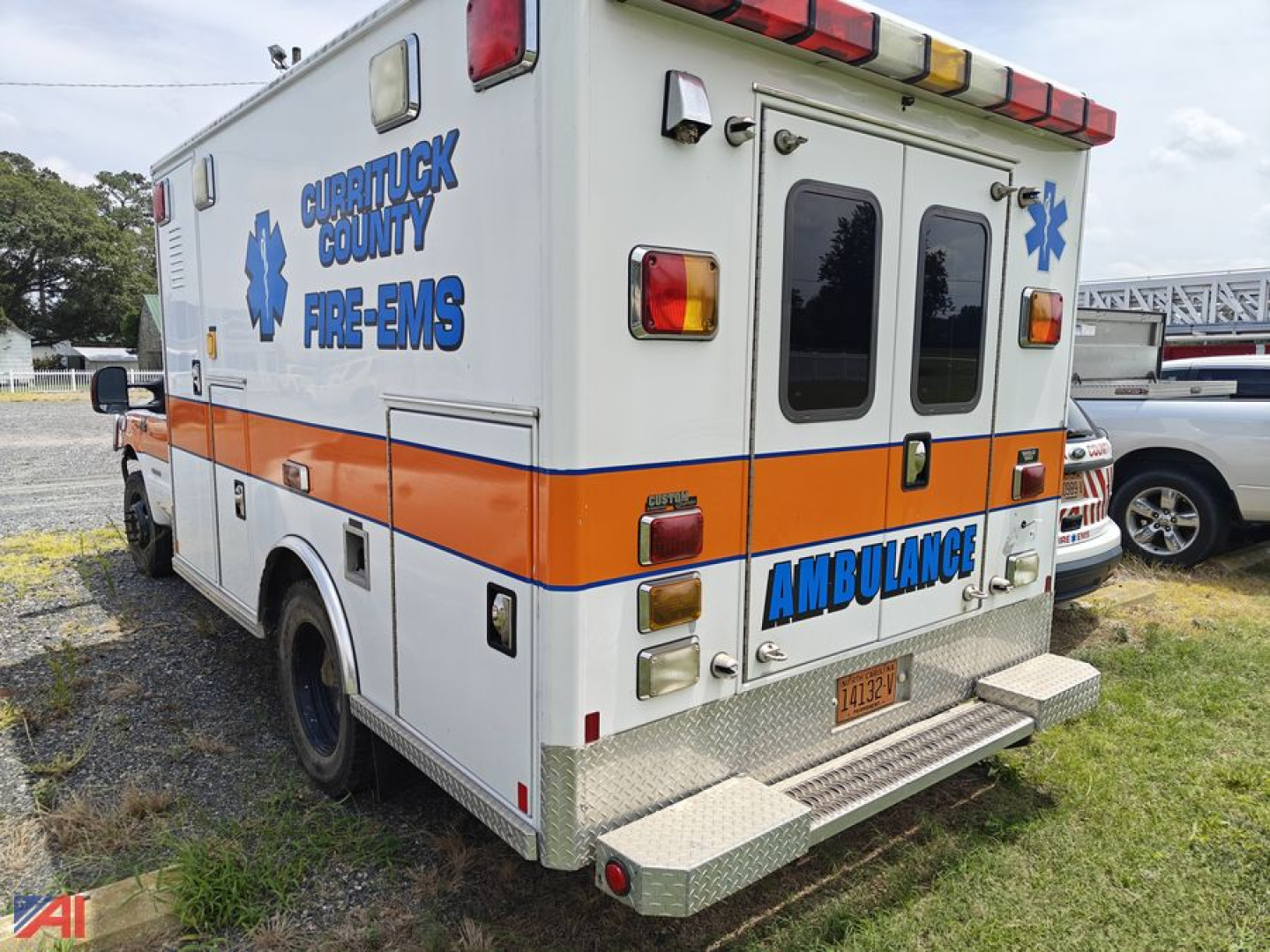 Ambulance rear view showing Currituck County Fire-EMS emblem and AMBULANCE text on white and orange body, rear doors, steps, and rear lights.