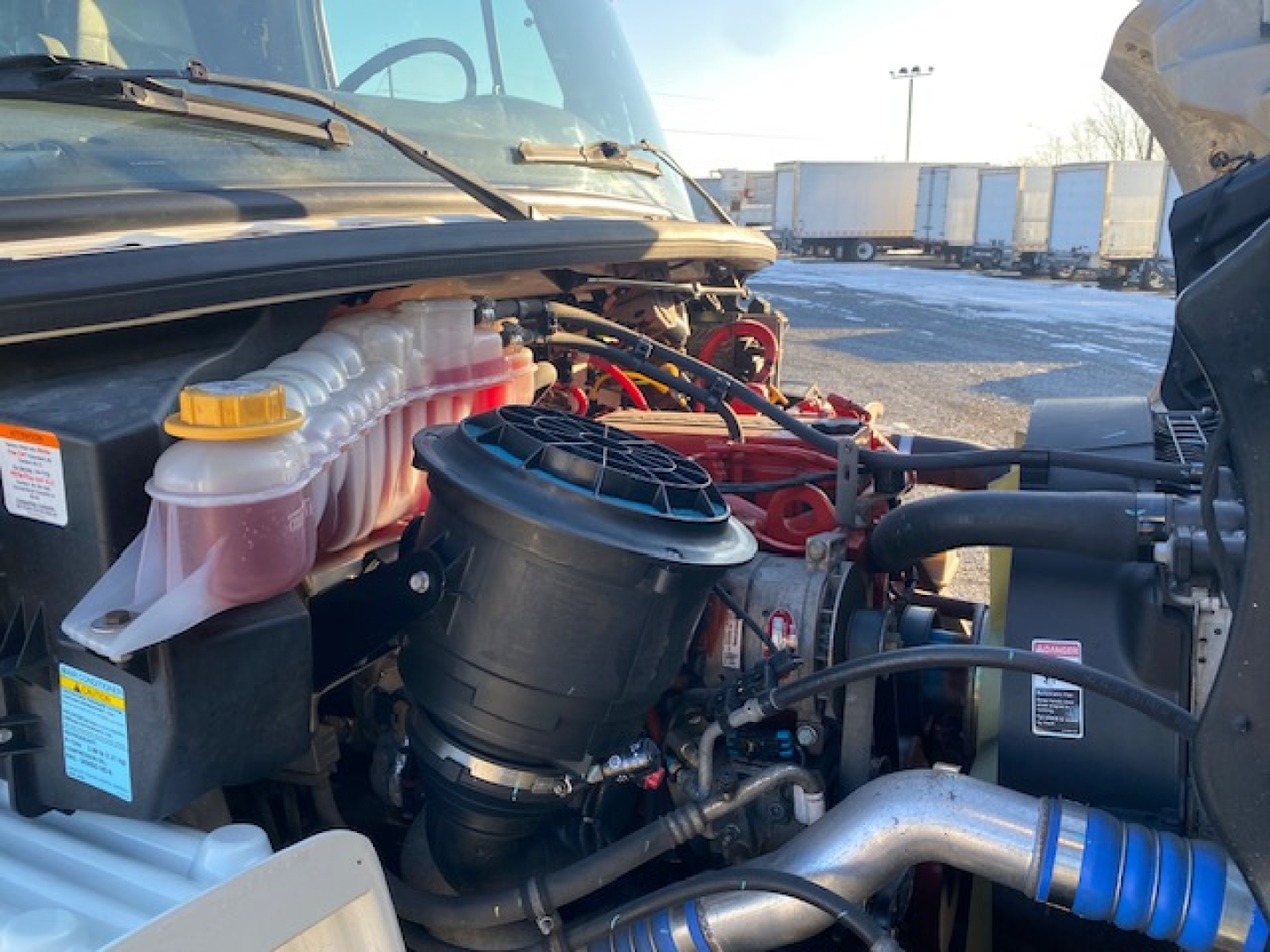Freightliner M2-106 engine bay showing coolant reservoir, black air filter housing, and various hoses.