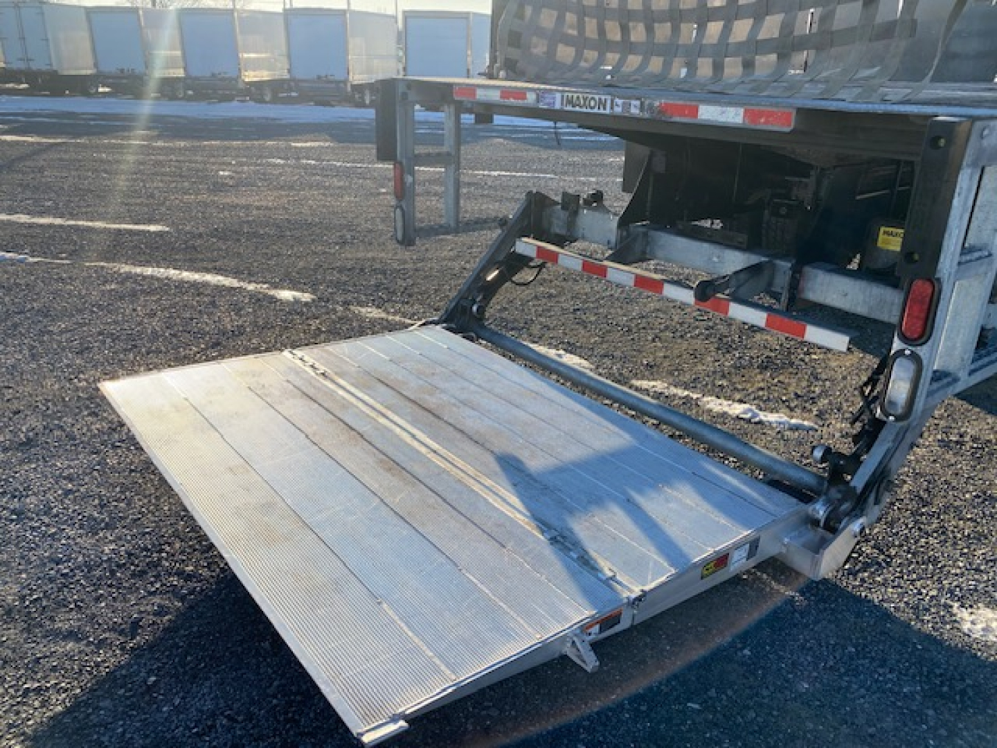 Freightliner M2-106 flatbed truck with extended aluminum ramp lowered showing rear deck and hydraulic lift, visible VIN and stock info in listing.