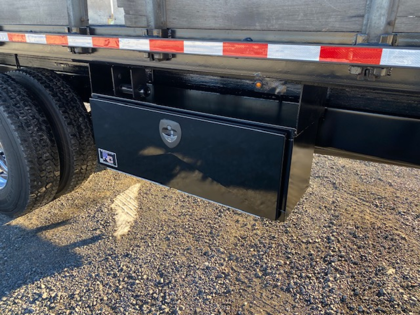 Flatbed Freightliner M2-106 undercarriage showing black tool/storage box mounted under trailer,”
