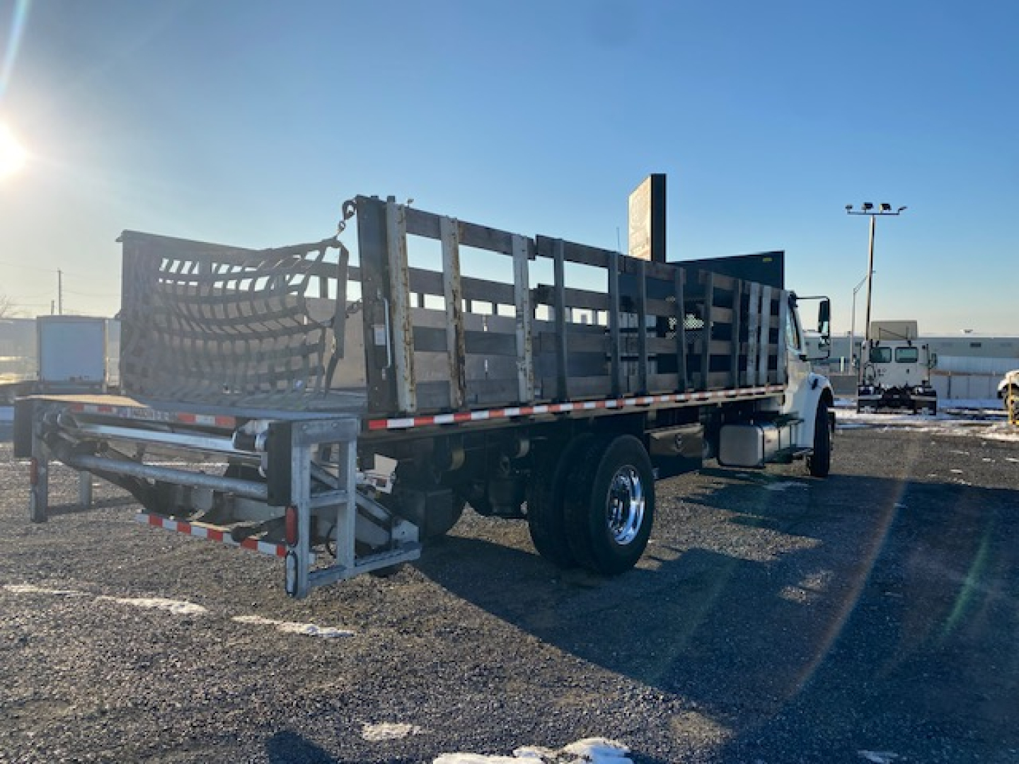 Flatbed Freightliner M2-106 truck with wood sides and metal railing, side view showing dual rear wheels and trailer bed.