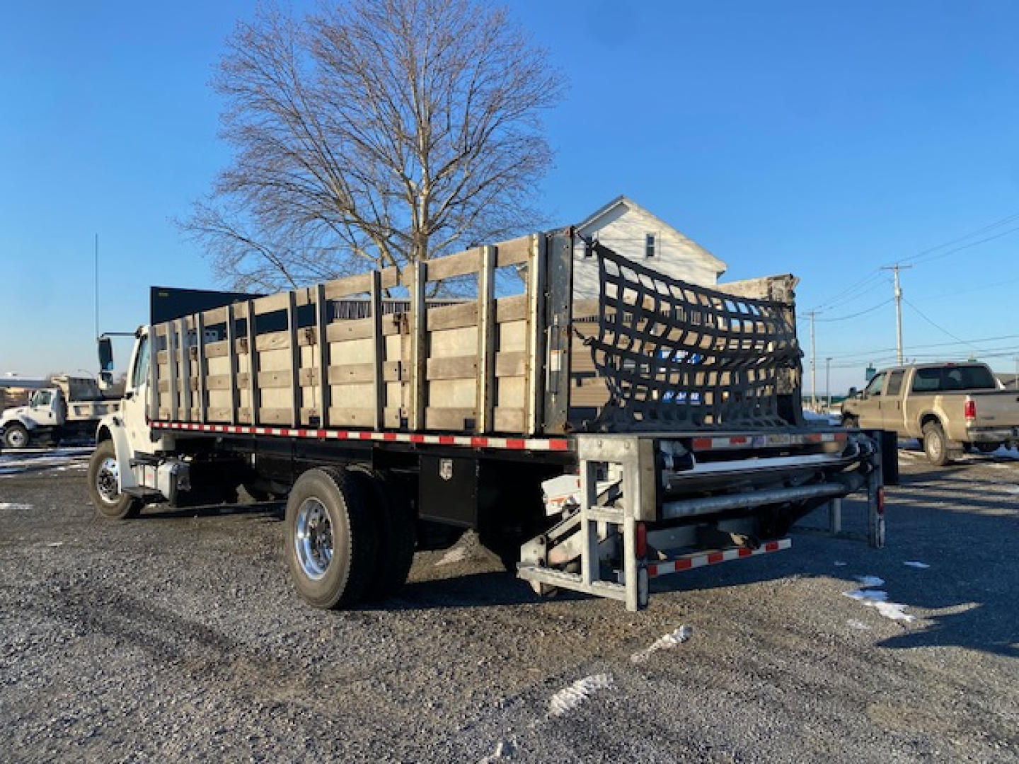 Freightliner M2-106 flatbed truck side and rear view showing wooden stake bed with metal supports and towing equipment.