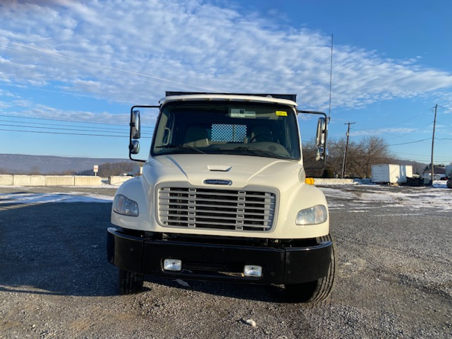 Front view of a white Freightliner M2-106 truck with a flatbed, large grille, rectangular headlights, and a black bumper.