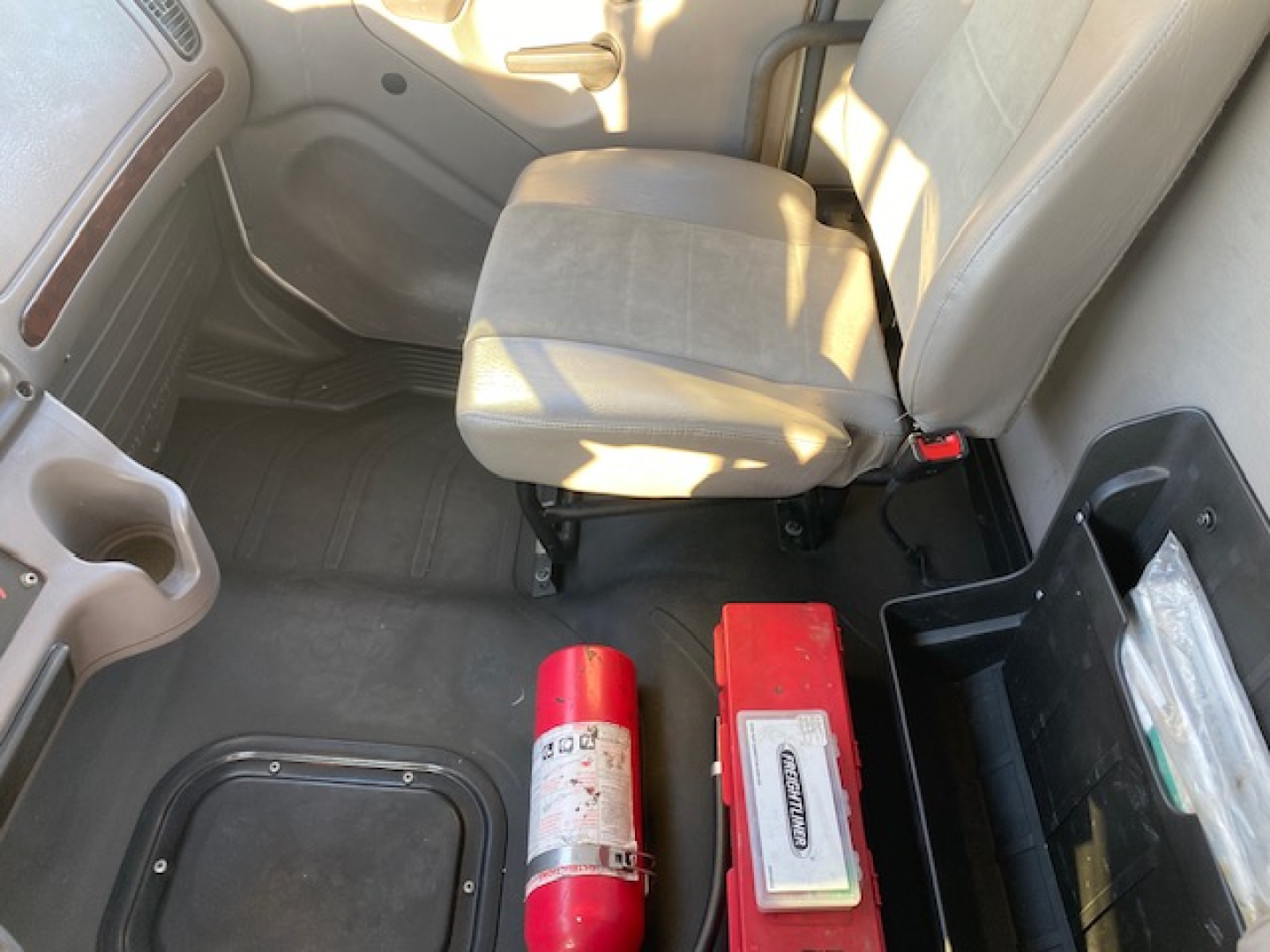 Interior cab of a 2020 Freightliner M2-106 showing front passenger seat, beige cloth upholstery, and two red safety devices on the floor beside a storage hatch.