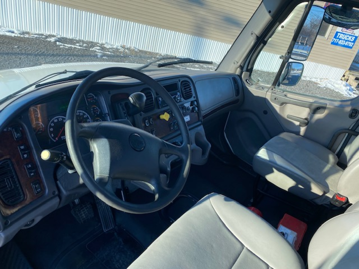 Freightliner M2-106 interior cabin view showing steering wheel, dashboard, and front seats.