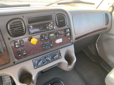  Freightliner M2-106 dashboard view showing radio, climate controls, and assorted switches; woodgrain panel with dials and cup holders visible.