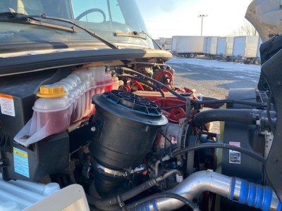 Freightliner M2-106 engine bay showing coolant reservoir, black air filter housing, and various hoses.