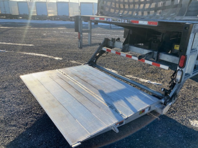Freightliner M2-106 flatbed truck with extended aluminum ramp lowered showing rear deck and hydraulic lift, visible VIN and stock info in listing.