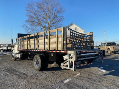Freightliner M2-106 flatbed truck side and rear view showing wooden stake bed with metal supports and towing equipment.
