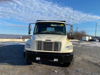 Front view of a white Freightliner M2-106 truck with a flatbed, large grille, rectangular headlights, and a black bumper.