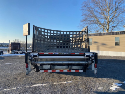 Freightliner M2-106 dump bed rear view showing black mesh tailgate and Maxon hydraulic mechanism, with reflective tape and lights.