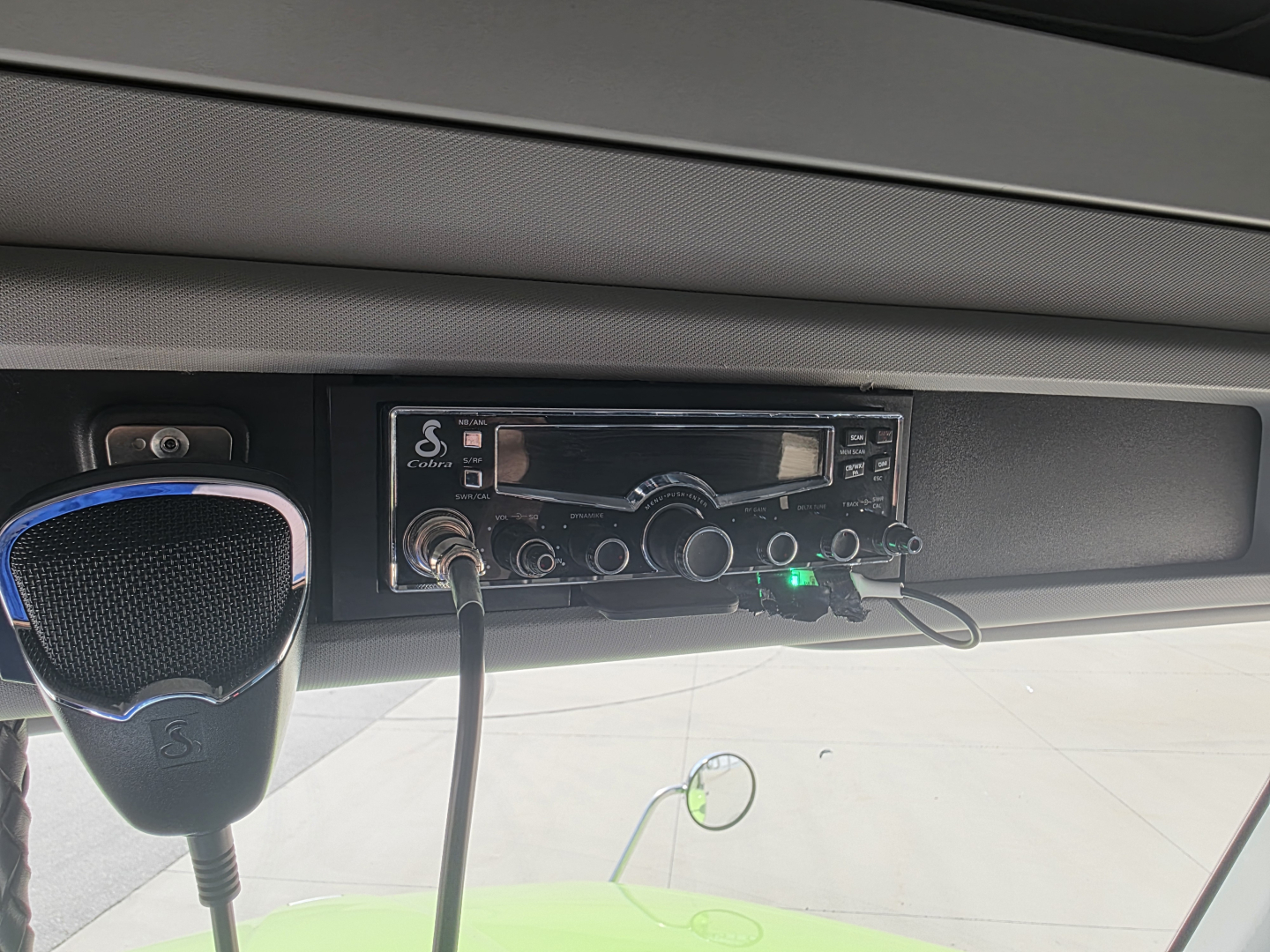 Truck cab interior showing Kenworth CB radio mic and audio head unit with controls; two cables plugged in; dashboard area.