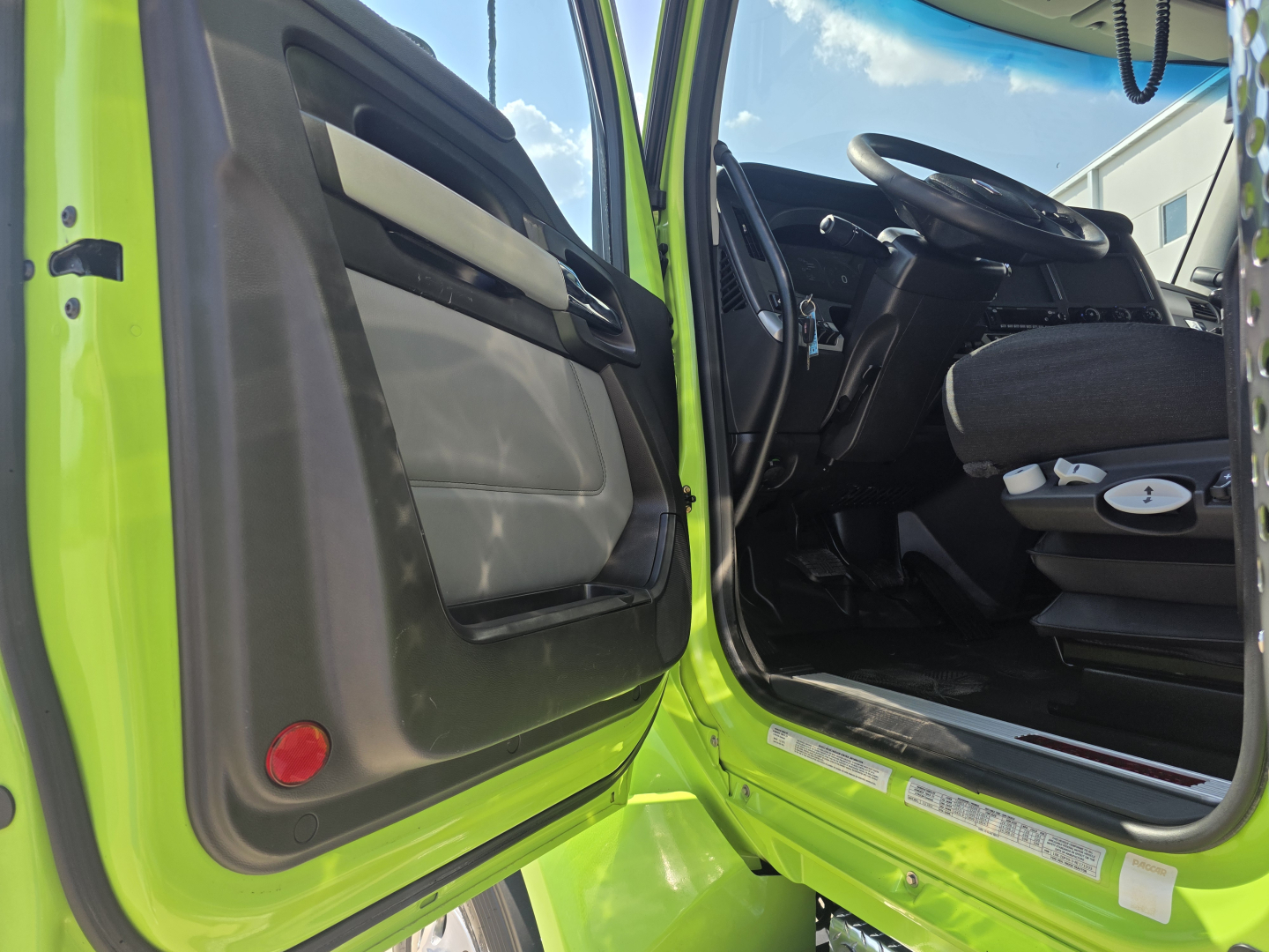 Kenworth T880 cab interior with open driver door, lime-green exterior, steering wheel, dashboard, and driver seat visible.