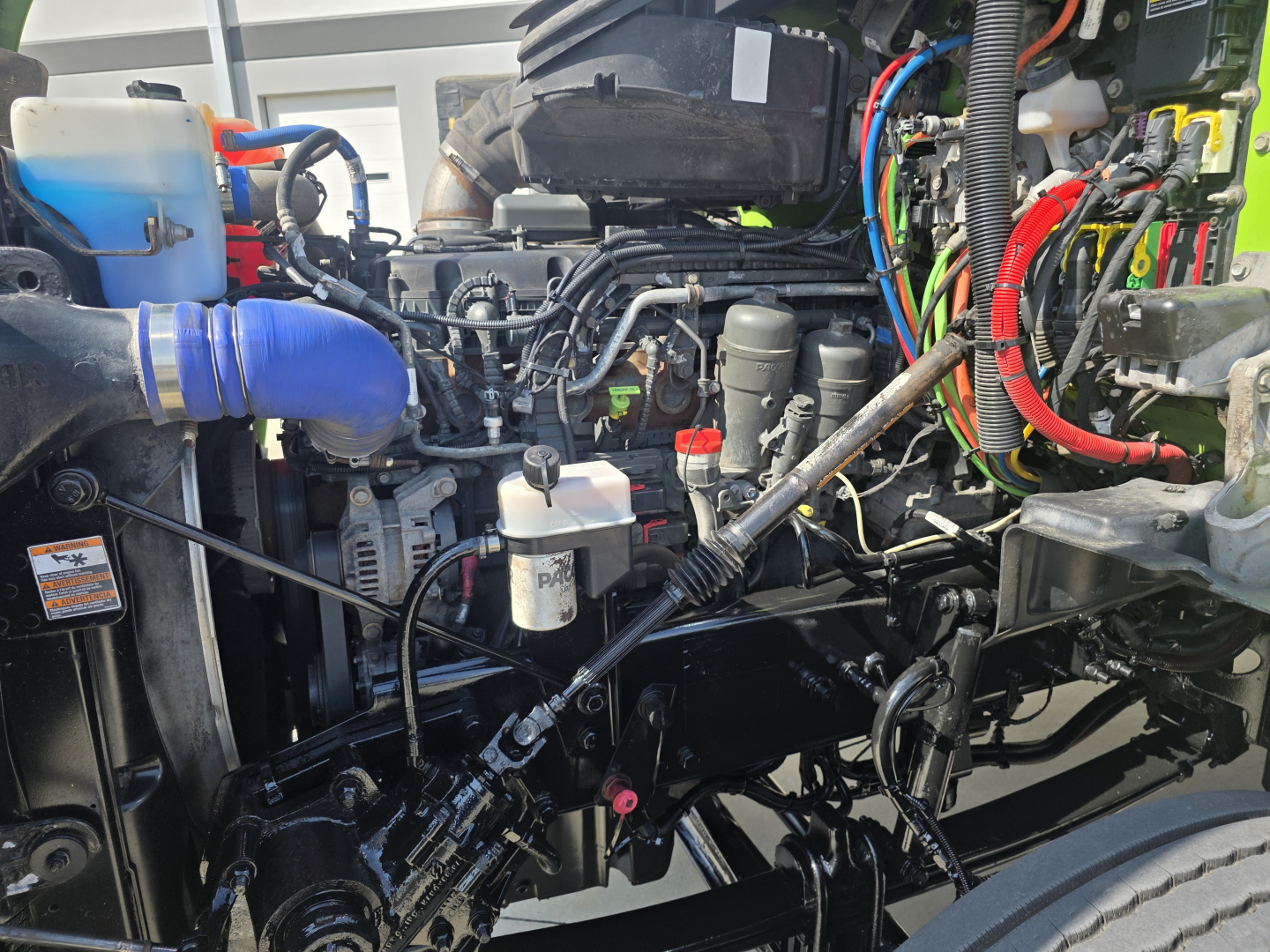 Kenworth T880 engine bay showing multiple hoses, wiring, and components including coolant reservoir, filter canister, and blue silicone hose.