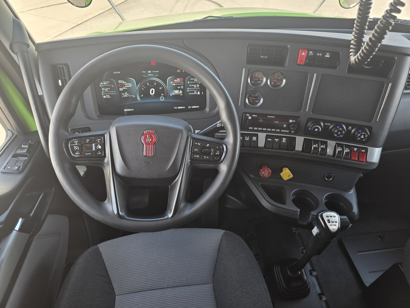 Kenworth T880 interior dashboard with steering wheel and gear shifter, digital instrument cluster, various controls, and a keypad, front cabin view.
