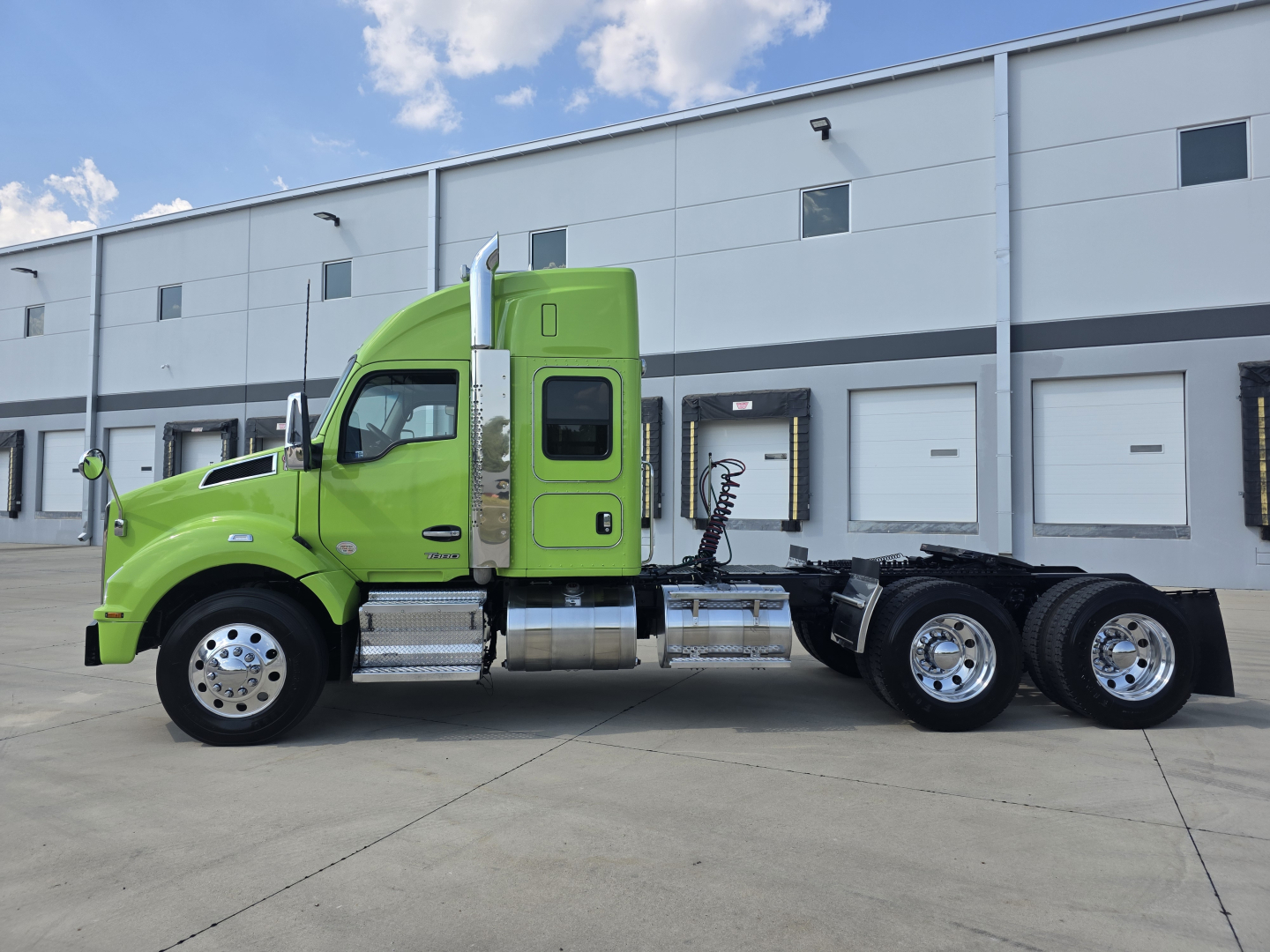 Green 2022 Kenworth T880 tractor side view showing cab, fuel tanks, rear axles, and wheel rims; no visible text on side other than door and cab features.
