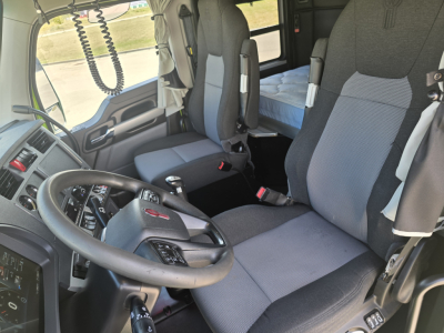 Kenworth T880 cab interior showing driver seat and passenger seat with grey fabric, steering wheel, dashboard, and bunk area.