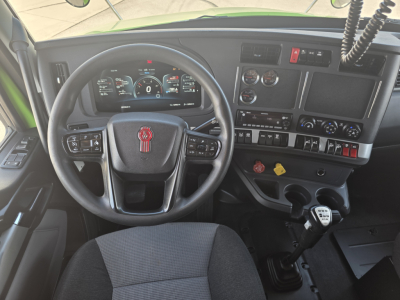 Kenworth T880 interior dashboard with steering wheel and gear shifter, digital instrument cluster, various controls, and a keypad, front cabin view.