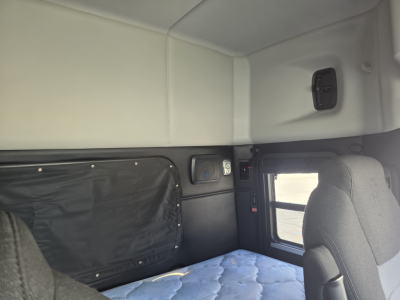 Interior sleeper cab of a 2022 Kenworth T880 showing side window, storage panel, and bed area with light-colored upholstery.