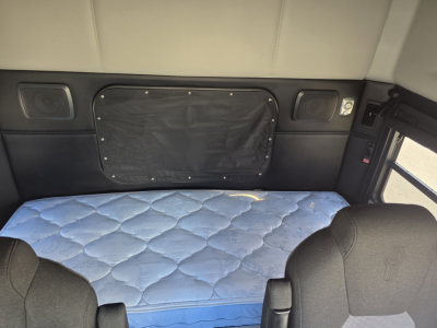 Kenworth T880 sleeper cab interior with a blue quilted mattress, black side panels, and overhead cabinet pockets visible in the sleeper area.