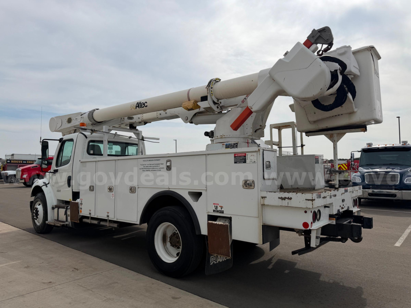 Truck mounted boom lift with Altec AM55 bucket truck extending from a utility service body, rear view showing stabilizers and work platform.