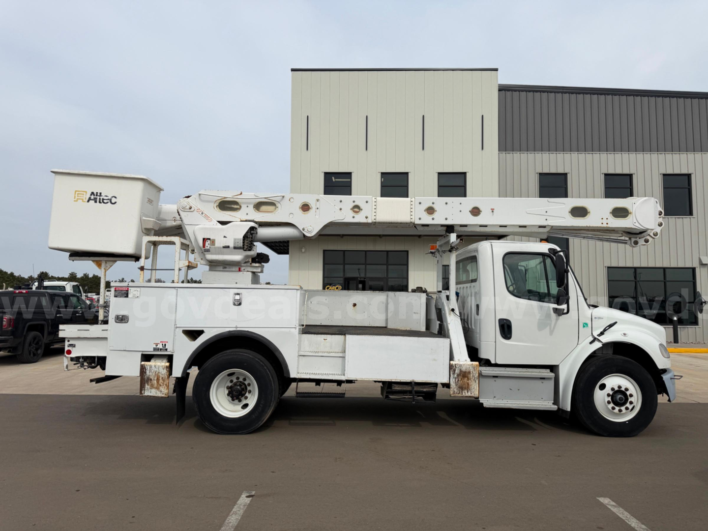 Freightliner Altec AM55 bucket truck in-service side view showing boom and utility body with stabilizers.