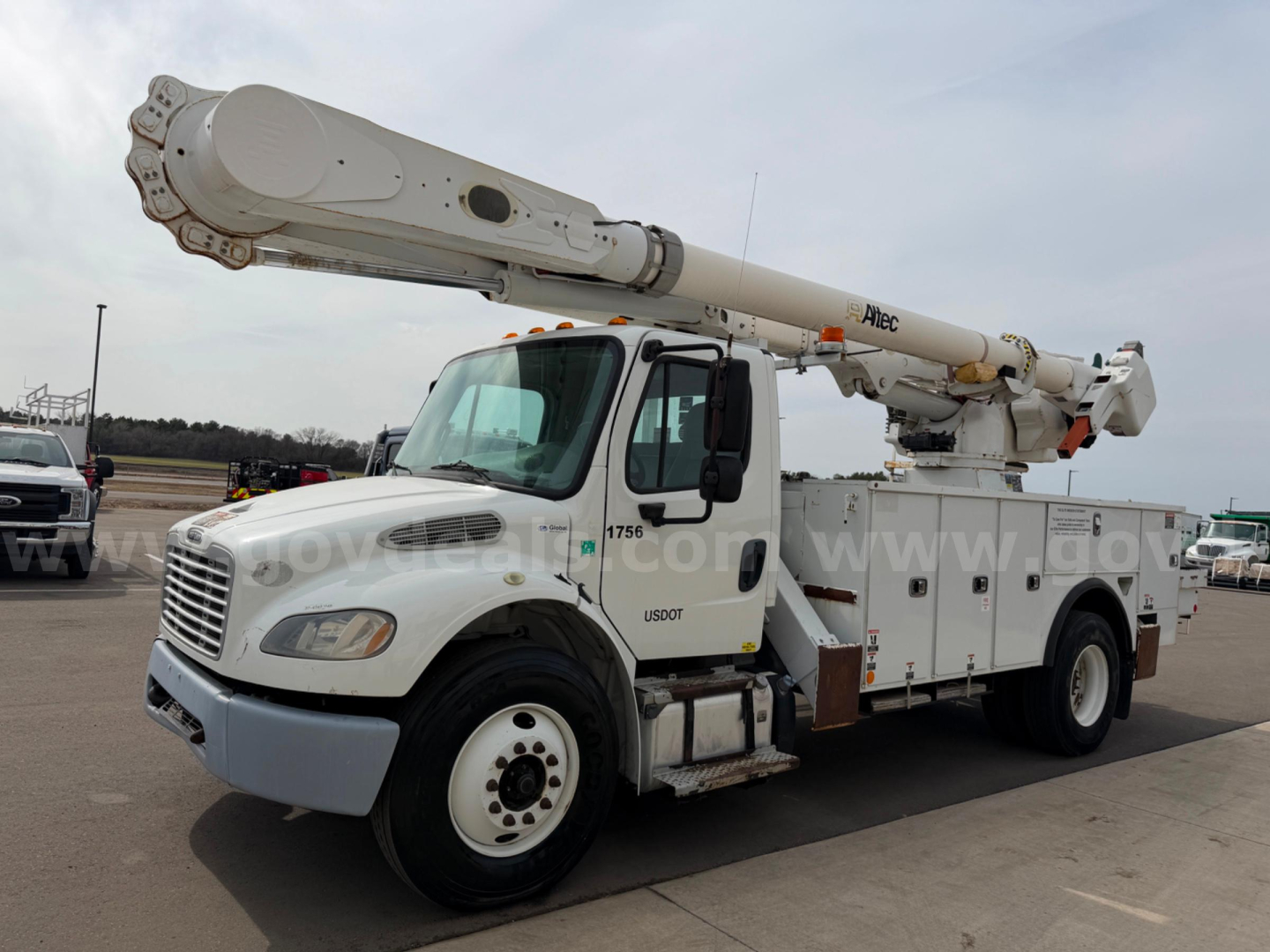 Bucket truck with extended boom on Freightliner chassis showing AM55 model equipment and utility compartments.