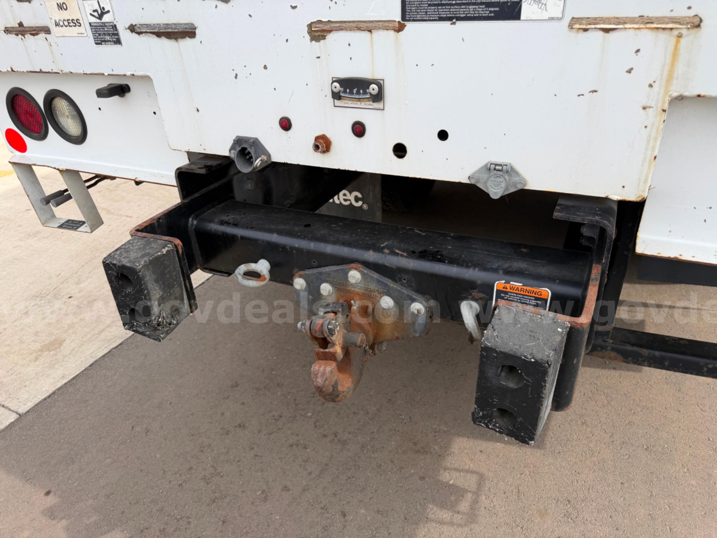 Rear view showing hitch and bumper of a Freightliner Altec AM55 bucket truck; visible hitch assembly, coupler, and two rectangular trailer receiver blocks; rust and wear on metal components.
