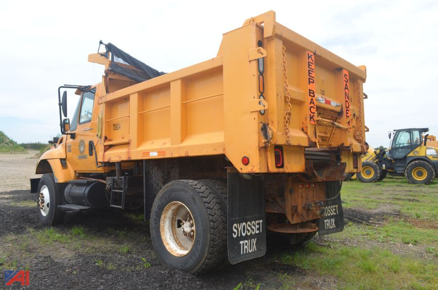 Dump truck rear view showing large orange dump bed, tailgate with chains, and mud flaps. Visible text includes 'SANDER' or 'SAND' on tailgate, 'SVOSET TRUX' on mud flaps, and some faded lettering on the side of the cab.