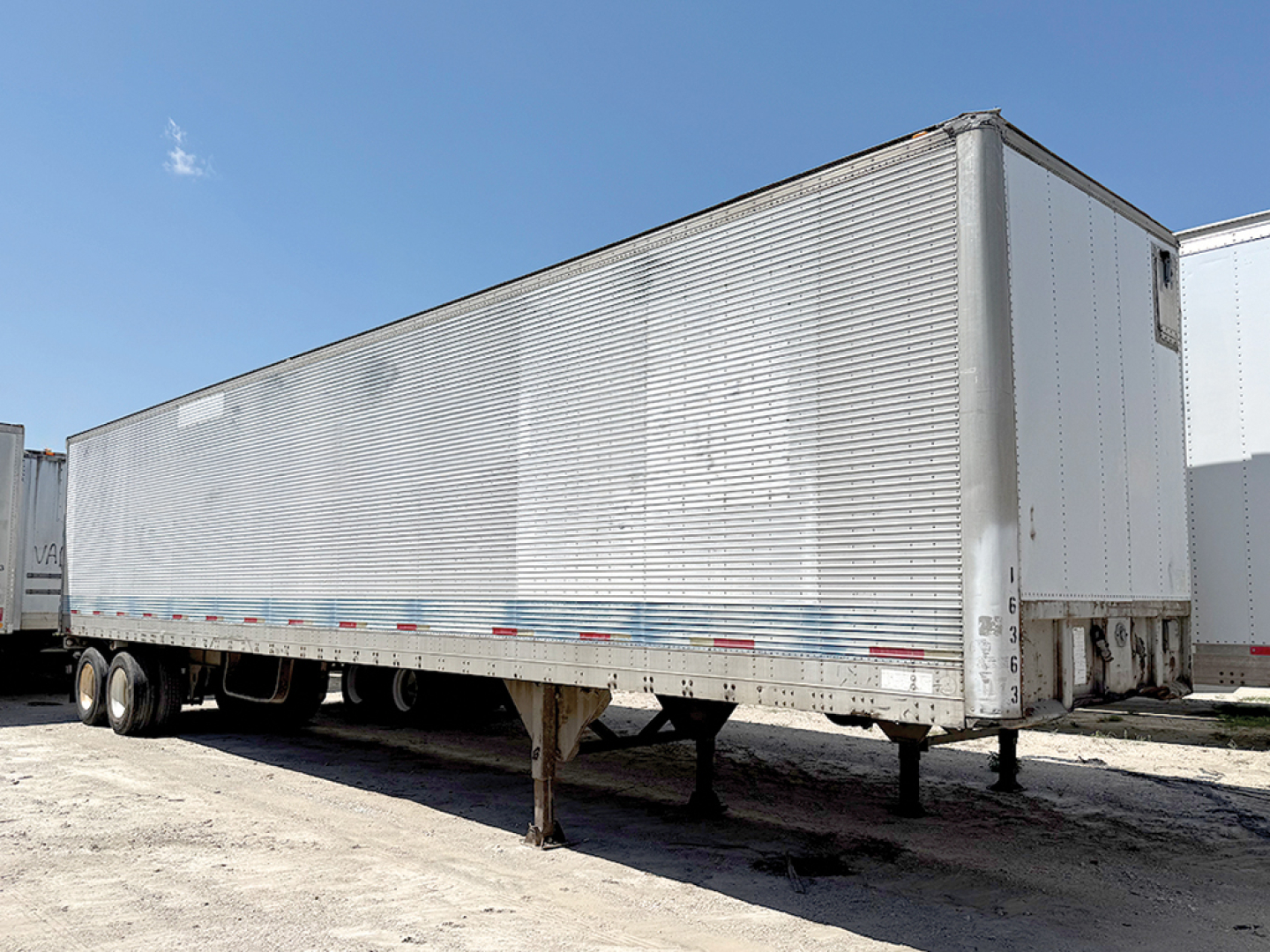 Trailer in a lot showing a long aluminum Hobbs van trailer with tandem axles and landing gear, side ribbed panels, no branding visible.