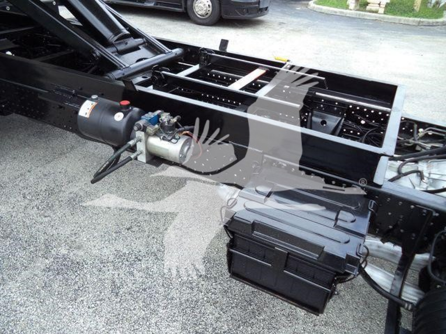 Isuzu NPR-HD truck chassis showing battery box and hydraulic motor assembly under flatbed frame.