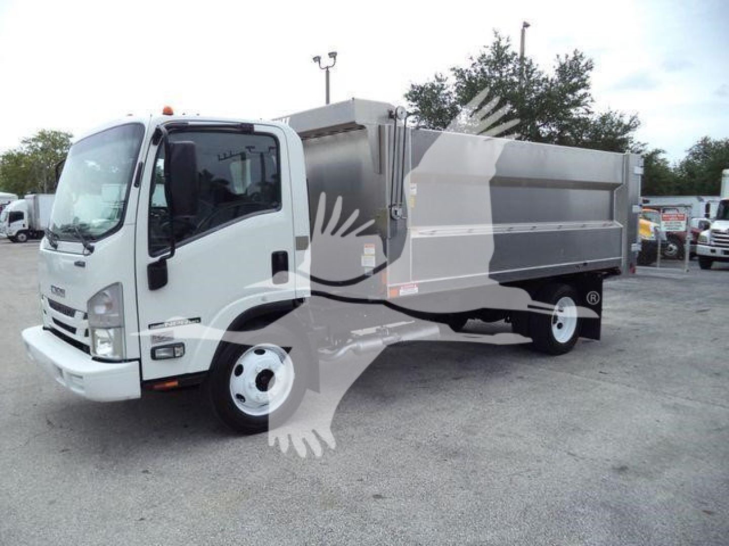Isuzu NPR-HD dump truck in a used inventory lot. Cab shows daytime running lights and side mirrors, with a large dumping bed.