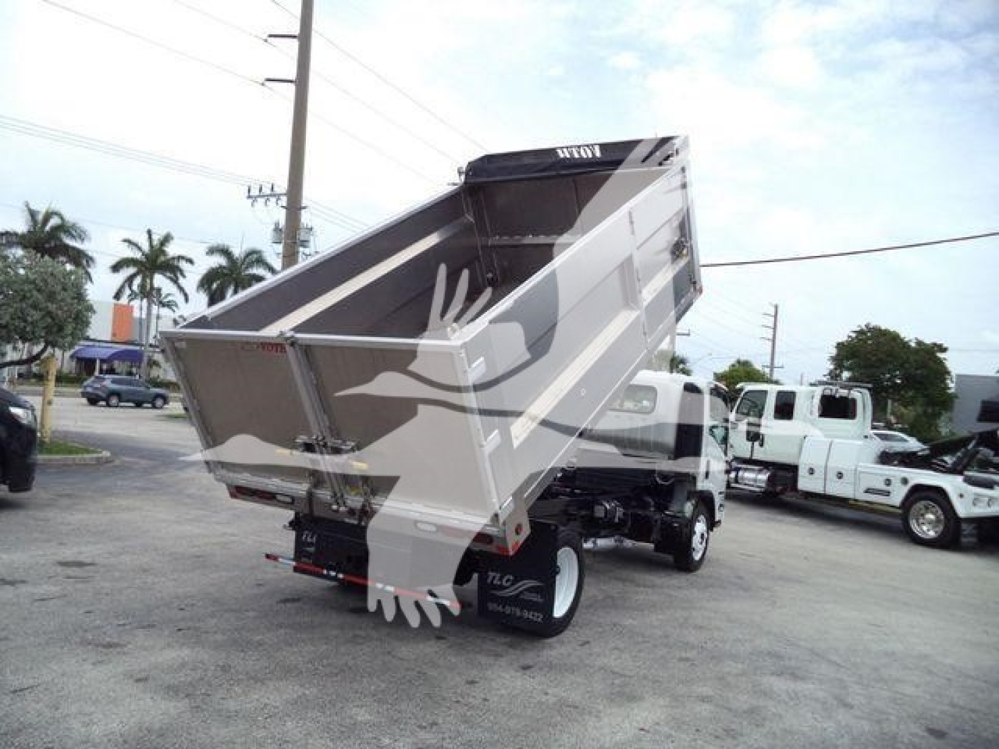 Isuzu NPR HD dump truck with raised metallic dump bed in a dealership lot. Visible text on sides includes Isuzu branding and numbers on wheel well.