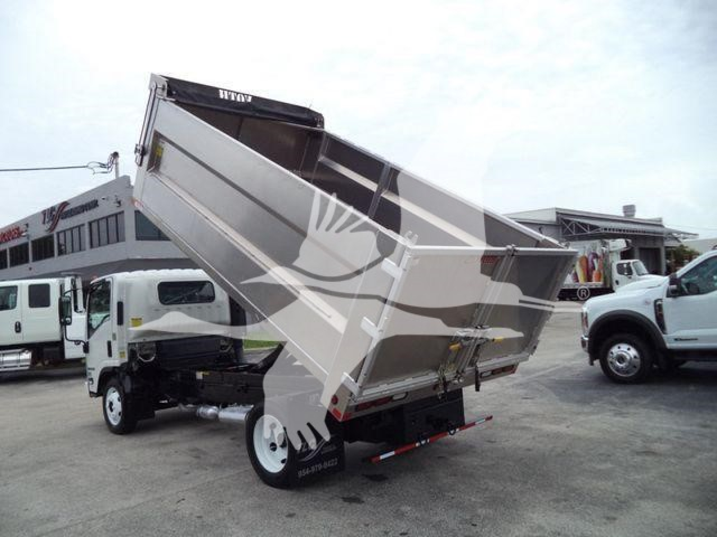 Isuzu NPR HD dump truck with bed partially raised, rear view showing hydraulic lift and dual rear wheels.