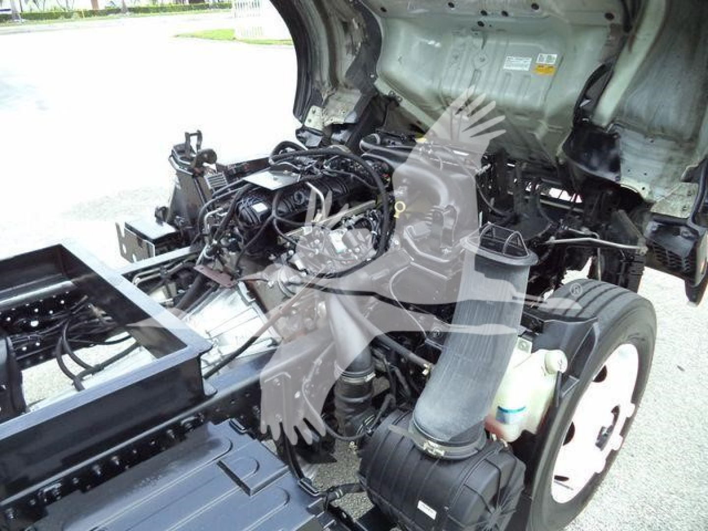 Isuzu NPR HD cab-over truck engine bay visible with exposed engine wiring and components; front wheel and intake ducting present.