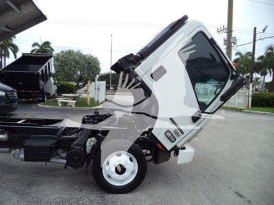Isuzu NPR HD cab forward truck chassis with cab tilted forward, showing front wheel and engine area; white body, black chassis, and hydraulic cab tilt mechanism visible.