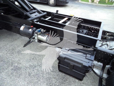 Isuzu NPR-HD truck chassis showing battery box and hydraulic motor assembly under flatbed frame.