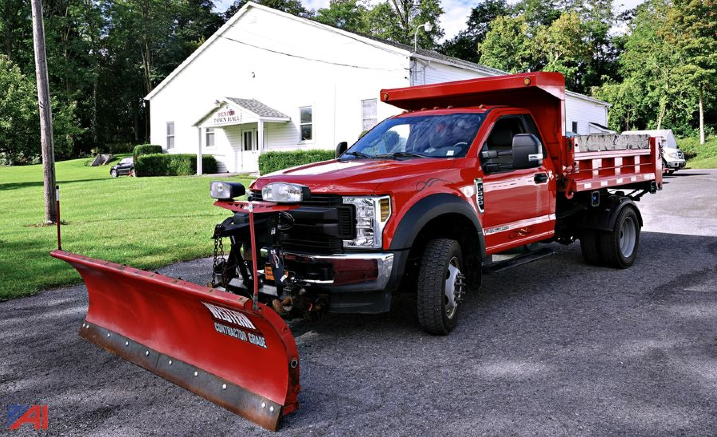 Ford F-550 dump truck with a front-mounted snow plow blade and red cab; side dump bed; GVW/utility truck in an outdoor lot.