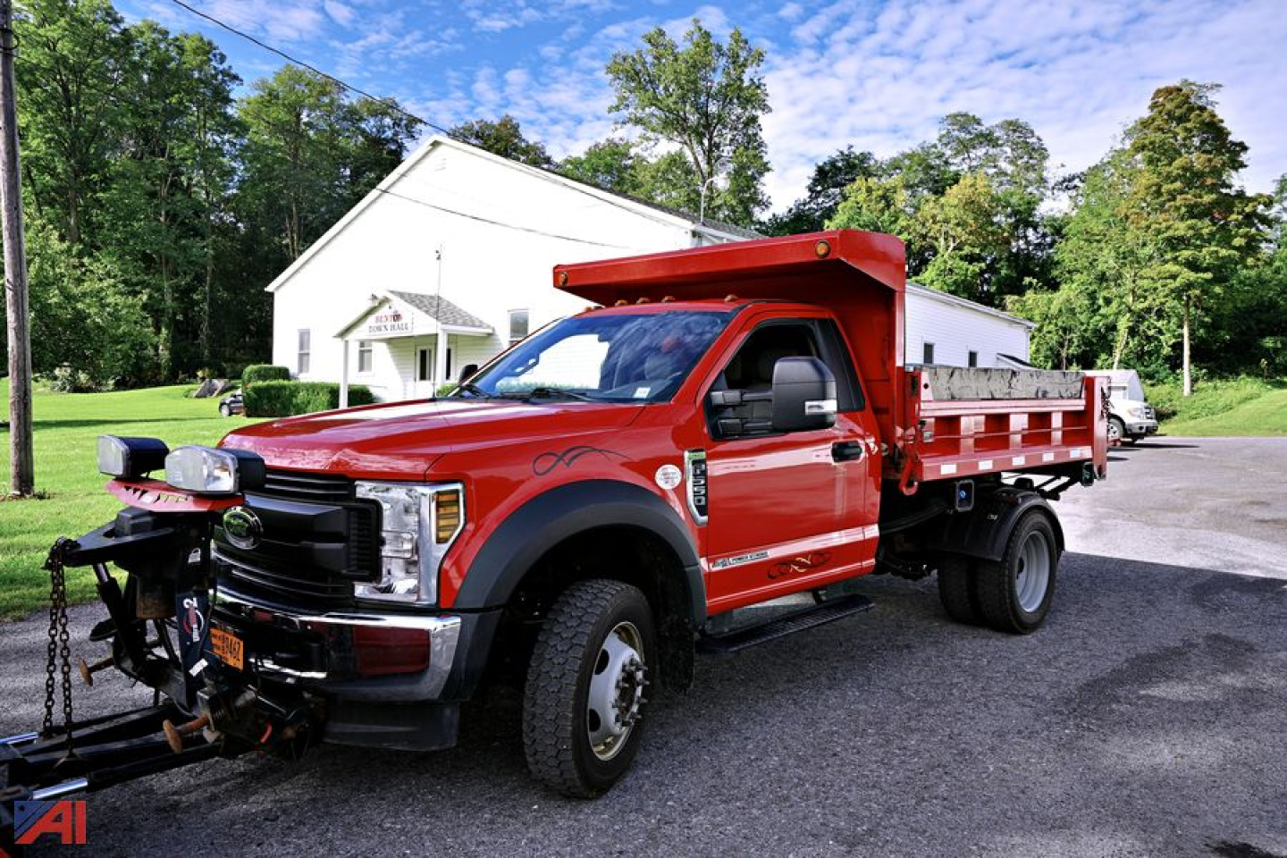 Ford F-550 dump truck with red cab and dump bed, front tow hitch, parked outdoors.