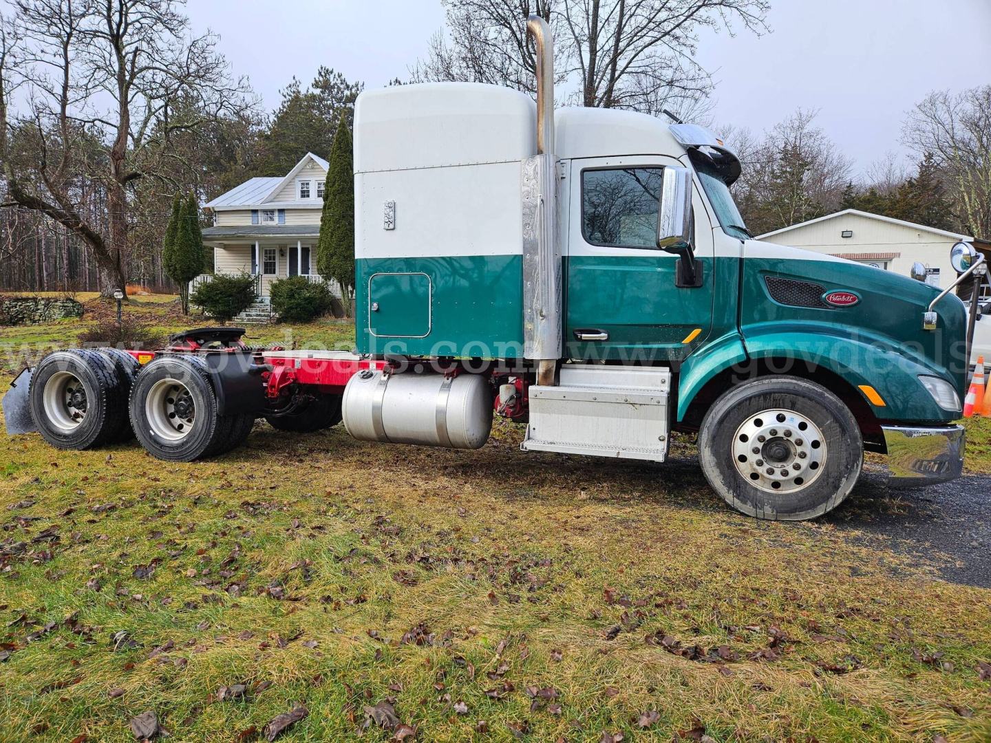 Peterbilt 579 truck side view showing cab and chassis with teal and gray color, diesel fuel tanks, dual rear axles, and exposed wheels.
