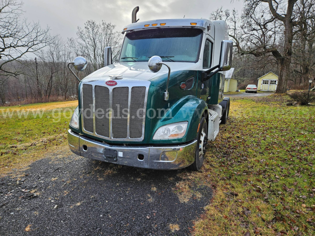 Peterbilt 579 truck front view showing chrome grille, dual large mirrors, and green/white cab with headlights and bumper.
