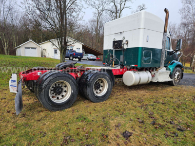 Peterbilt 579 truck chassis with dual rear axles, green and white cab, exposed exhaust, fuel tanks, and red frame visible in a rural lot.