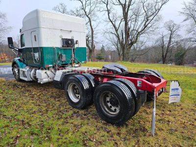 Peterbilt 579 tractor with green and white cab, showing rear chassis and dual rear wheels; visible are fuel tanks, fifth wheel, and a small sign in ground.