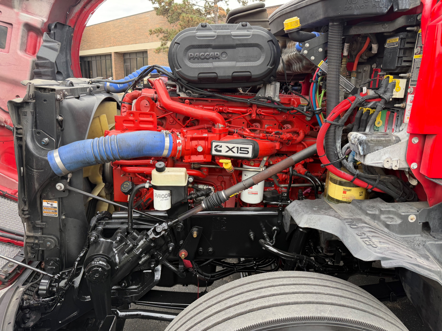Kenworth T680 engine bay showing Cummins X15 label and red engine components with blue turbo intake hose.