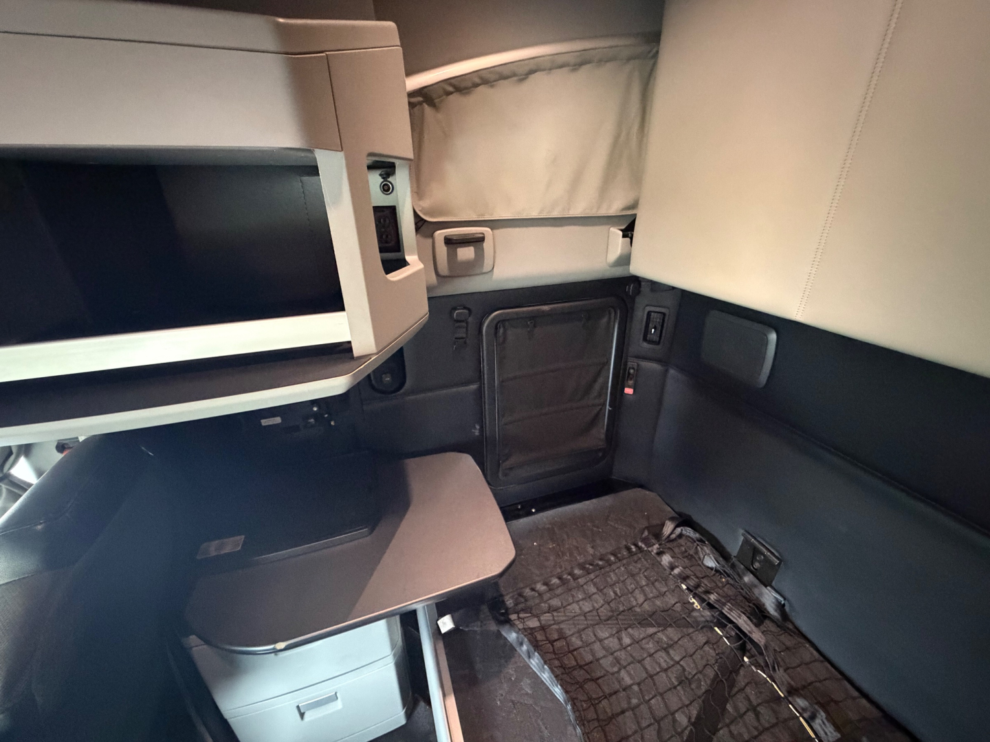 Interior of a Kenworth T680 sleeper cab showing a mounted microwave, a fold-out table, and seating area with storage compartments.