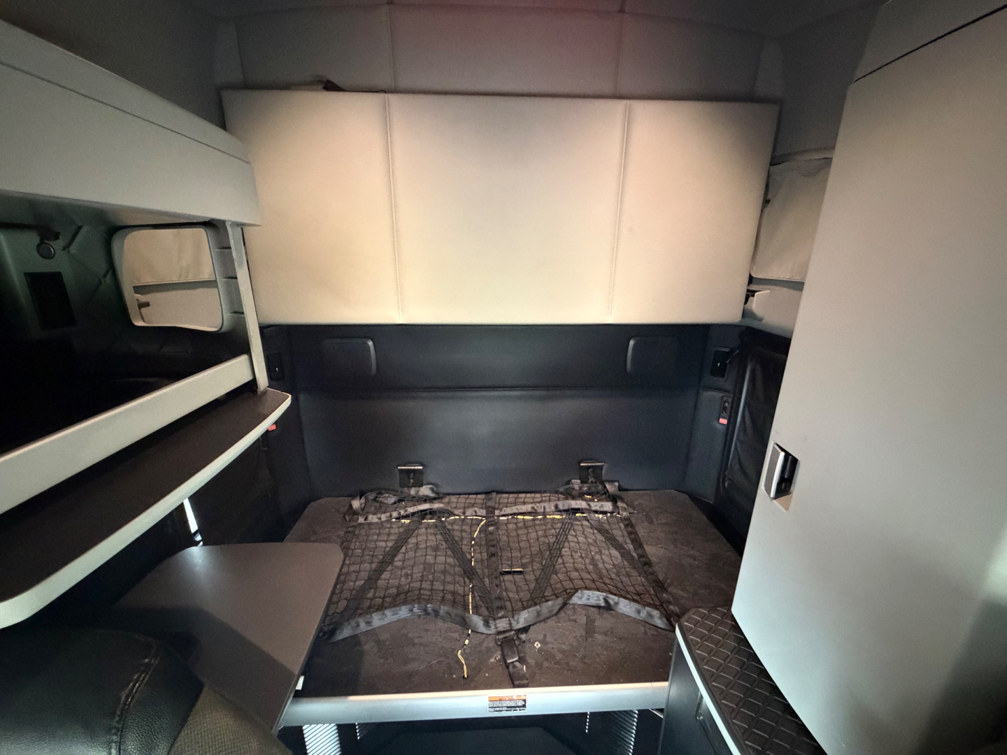 Kenworth T680 sleeper cab interior showing storage shelves, netted bed area, and side cabinet.