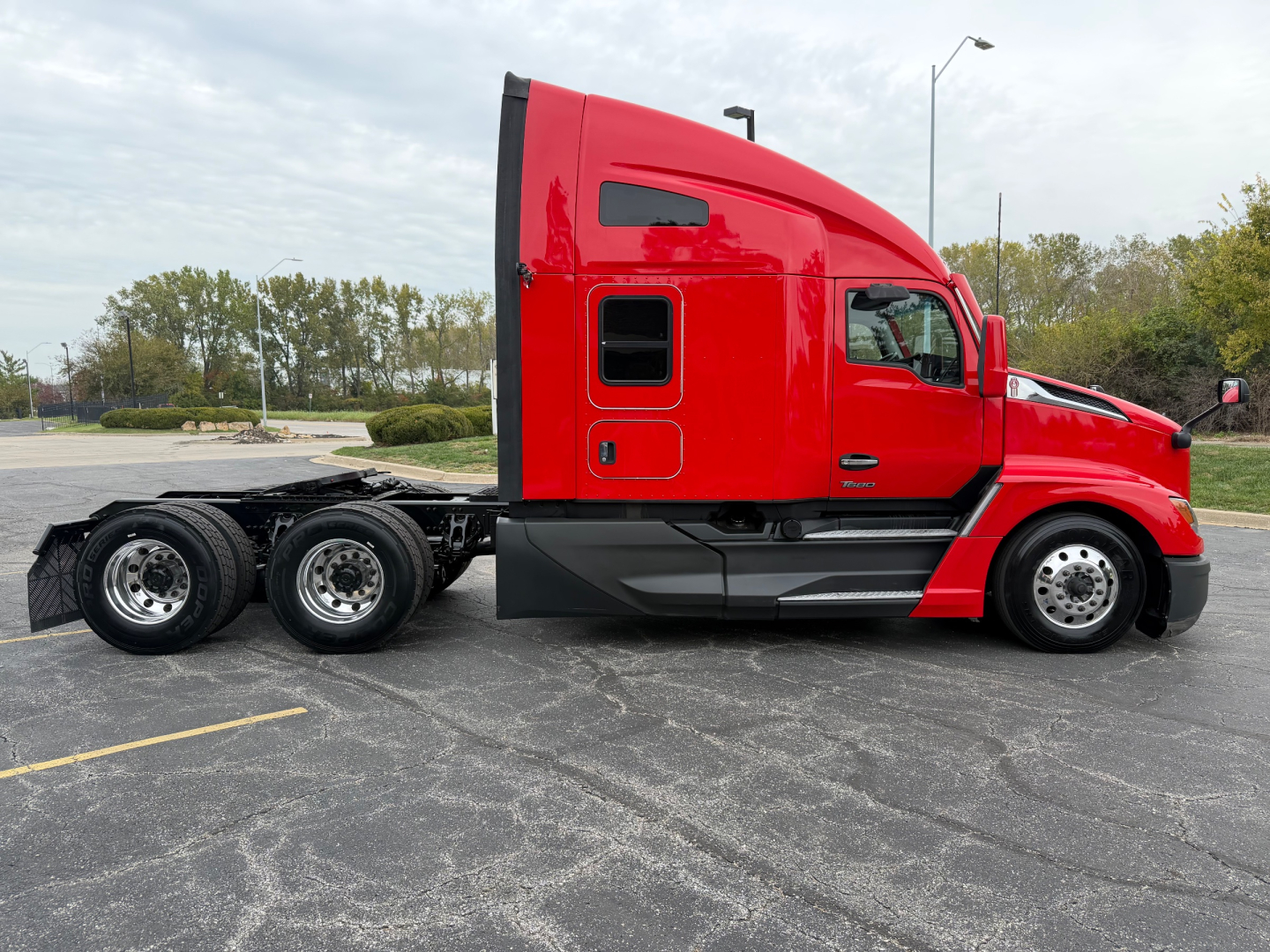 2023 Kenworth T680 side view showing sleeper cab and rear dual axle tractor chassis with red paint and black frame.